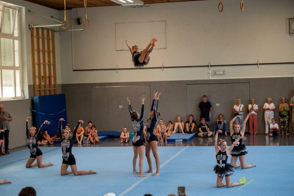 Akrobatische Darbietung einer Gruppe von Turnerinnen in einem Hallenraum.