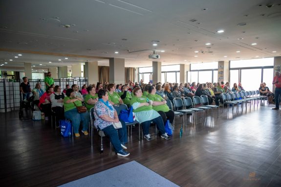 Eine Gruppe von Menschen sitzt in einem heller Raum mit großen Fenstern.