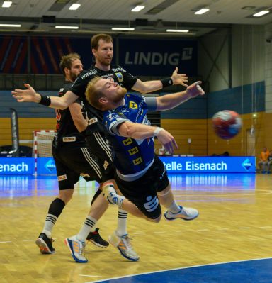 Handballspieler springt, um den Ball zu werfen, während zwei Verteidiger reagieren.