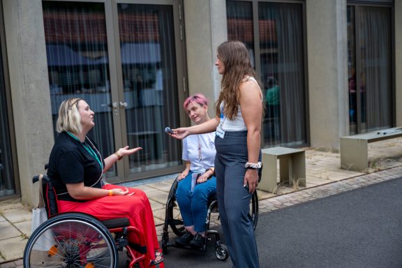 Drei Frauen im Gespräch, zwei im Rollstuhl, eine steht daneben. Freundliche Atmosphäre.