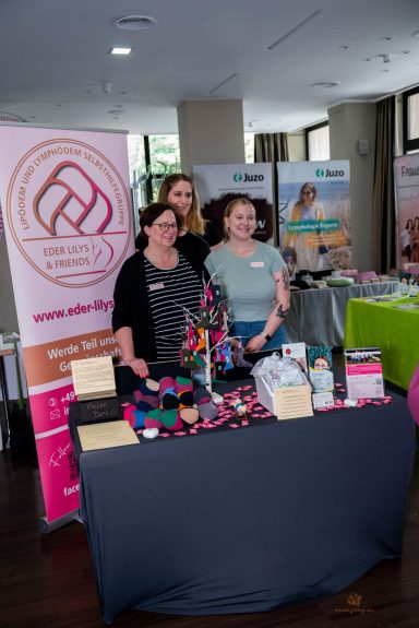 Drei Frauen am Messestand mit bunten Produkten und Werbematerialien.