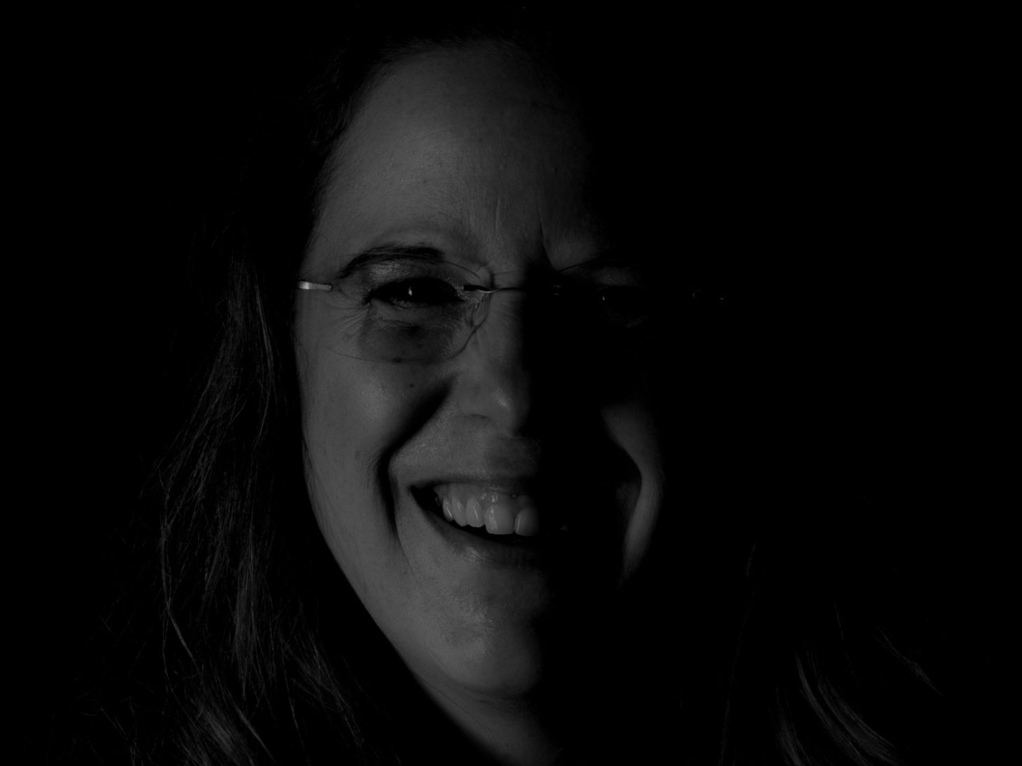 Lächelnde Person mit Brille vor dunklem Hintergrund.